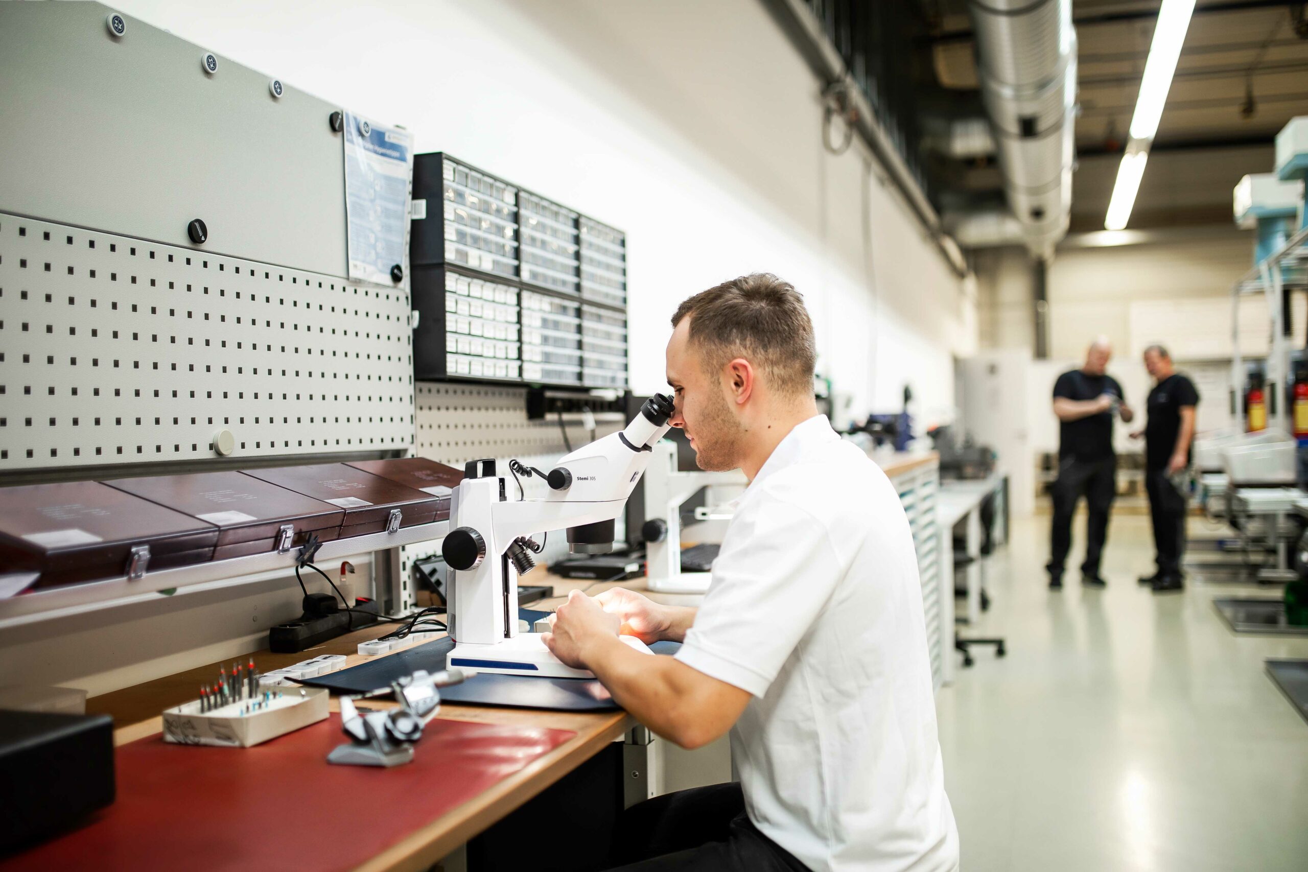 Ein Mitarbeiter in weißem Polo-Hemd schaut durch ein Mikroskop